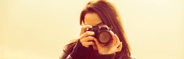 young woman using a camera to take photo outdoors retro colors